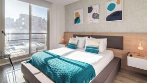 Ein modernes Schlafzimmer mit einem großen Bett, Blick auf Gebäude durch ein großes Fenster und abstrakte Kunst an der Wand.