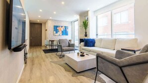 Ein modernes Wohnzimmer mit Flachbildfernseher, einer Couch, einem Couchtisch und einem Essbereich mit Tisch und Stühlen.