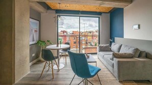 A modern living room with a sofa, a dining table with chairs, and a large window with a city view. - NOK Bright Loft in Chapinero (Bogotá)