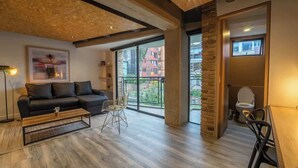 A modern living room with a black leather sofa, a wooden coffee table, and a dining area with a table and chairs. Large windows provide a view of the outside. - NOK Stunning 1 Br in Chapinero (Bogotá)