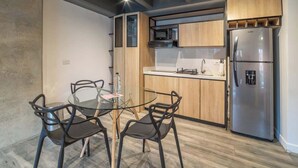 A modern kitchen with wooden cabinets, a stainless steel refrigerator, and a glass dining table with black chairs. - NOK Stunning 1 Br in Chapinero (Bogotá)