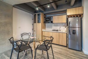 Eine moderne Küche mit Holzausstattung, einem Edelstahl-Kühlschrank und einem Glastisch mit schwarzen Stühlen.