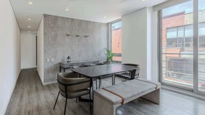 A modern kitchen with a large island, dark wood flooring, and a view of the city through large windows.
