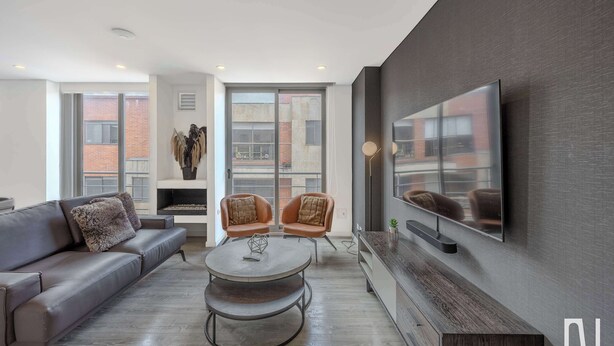 A modern living room with a sofa, two armchairs, a coffee table, and a TV mounted on the wall.