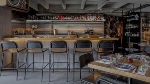 Un área de bar con mostrador de madera, taburetes y una variedad de botellas.
