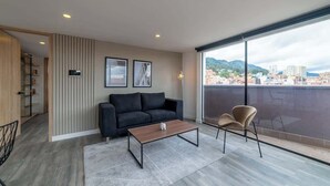 Una sala de estar moderna con un sofá, una mesa de centro y sillas, un ventanal con vistas a la ciudad y un mueble de madera.