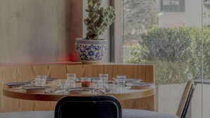 Comedor con mesa lista para cuatro personas, una planta en maceta y un colgador de luz.