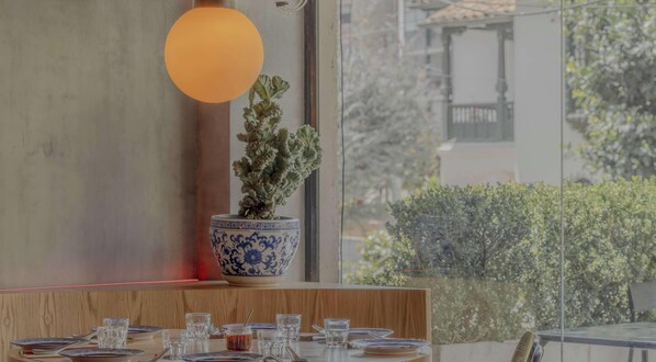 Een eethoek met een ronde tafel gedekt voor vier personen, een kamerplant en een groot raam met uitzicht op groen.