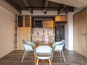 Een moderne keuken met houten kastjes, een magnetron en een koelkast. Op de voorgrond staat een glazen tafel met twee stoelen.