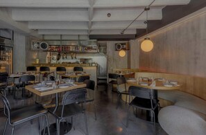 A restaurant interior with tables, chairs, a bar area, and pendant lighting.