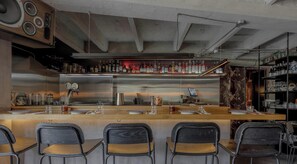 A bar area with a stainless steel bar counter, multiple bar stools, and a variety of bottles and glasses on shelves.