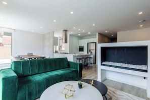 A modern living room with a green sofa, a round coffee table, and a large flat-screen TV mounted on the wall.