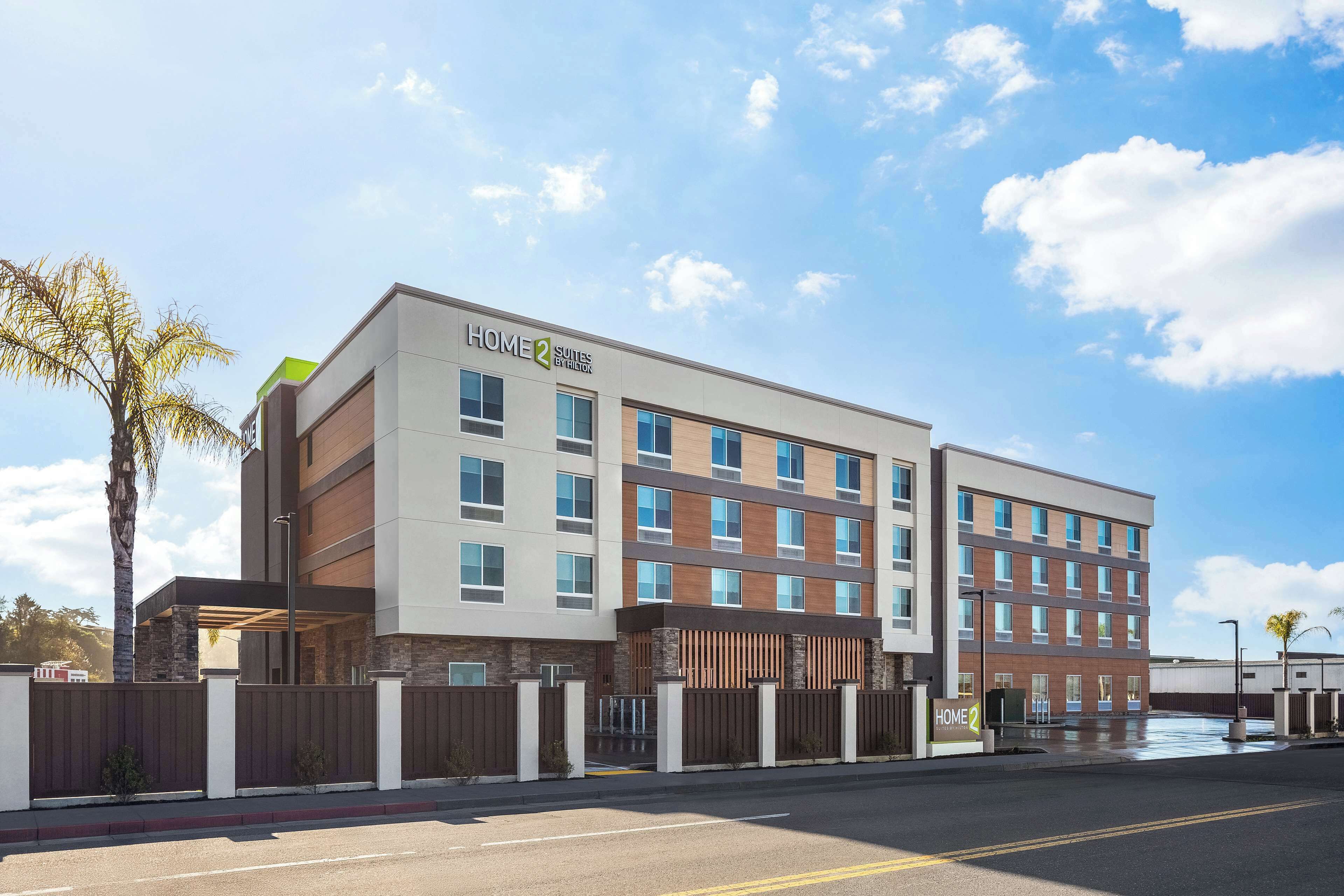 A modern hotel building with multiple floors, a gated entrance, and a clear sky.