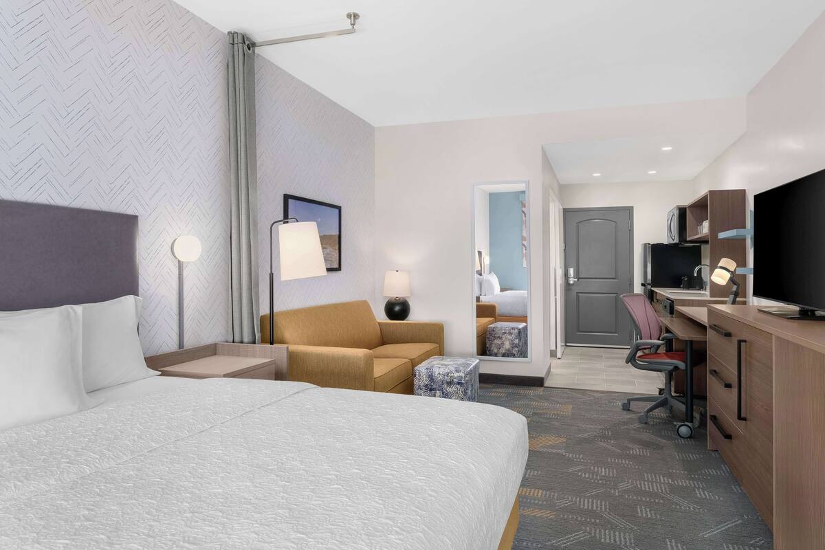 Ein Hotelzimmer mit einem großen Bett, einer Sitzecke, einem Schreibtisch mit Computer und einem Fernseher.