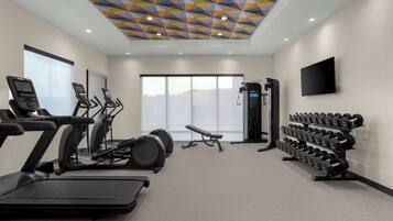A gym with treadmills, elliptical machines, a bench, and a rack of dumbbells.