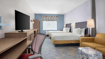 A hotel room with a desk, two beds, a TV, a chair, and a lamp.