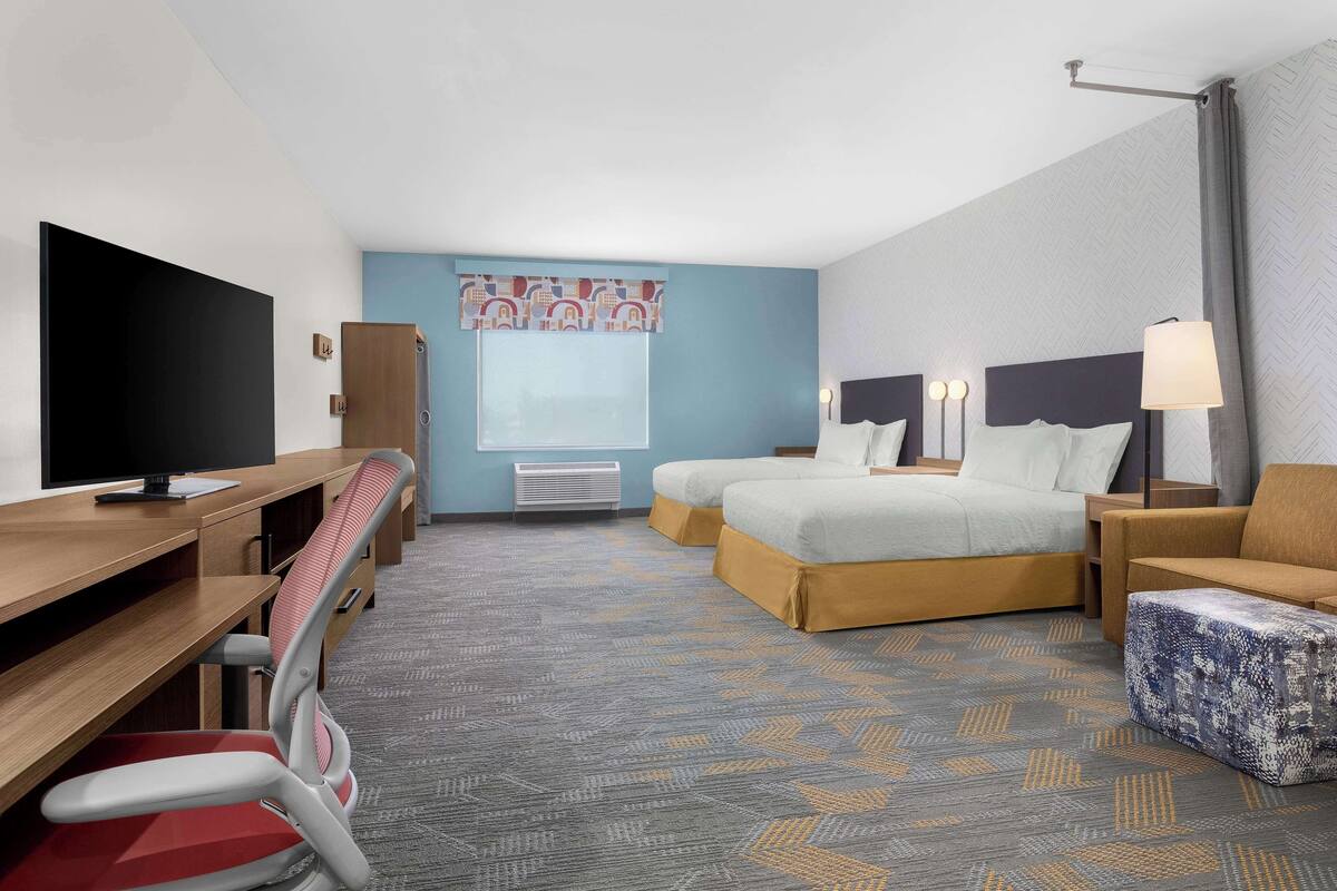 Ein Hotelzimmer mit Schreibtisch, Fernseher, zwei Betten, einer Couch und einem gemusterten Teppich.