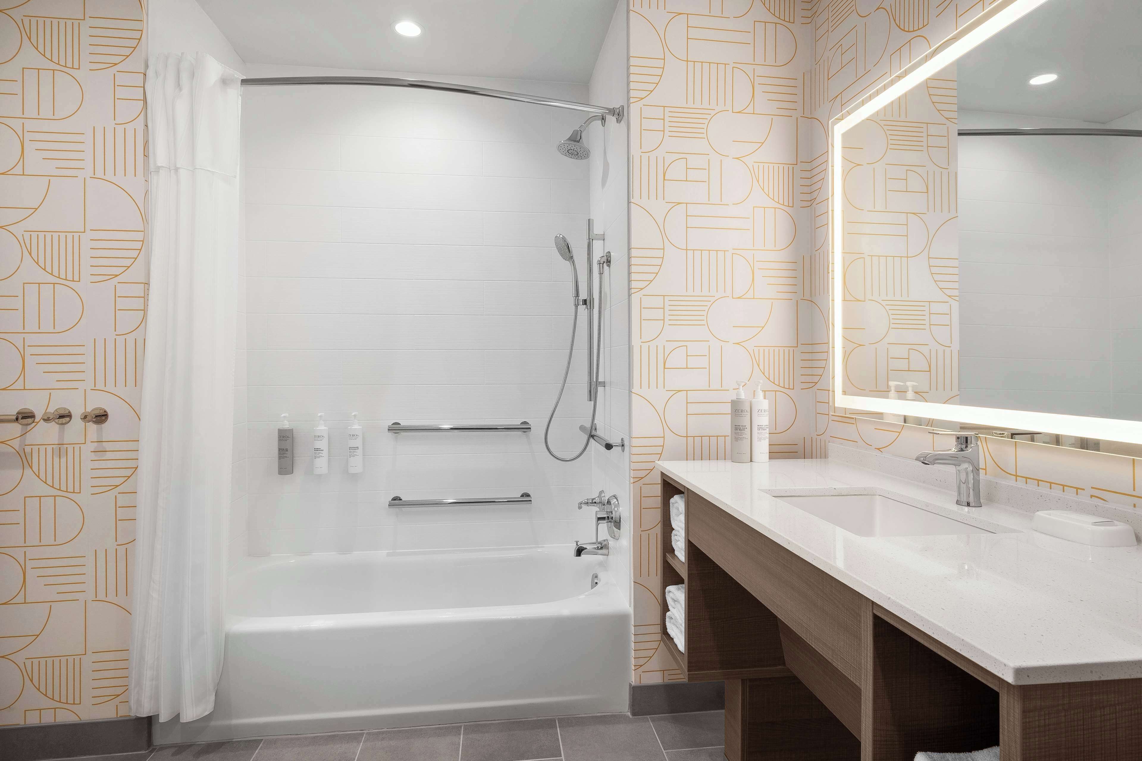 A modern bathroom with a bathtub, shower, and vanity with a mirror.