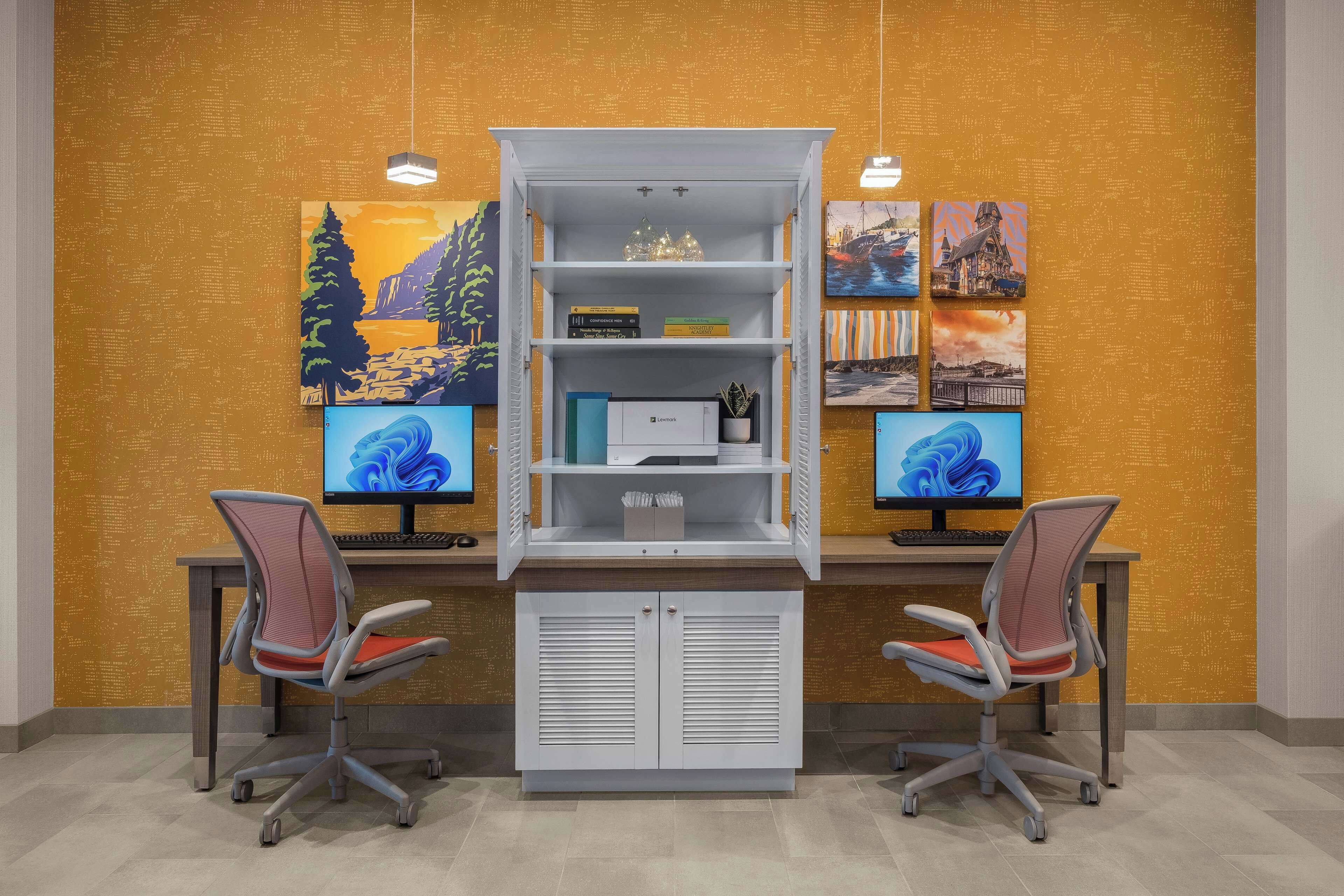 A workspace with two desks, each with a computer monitor, a chair, and a white shelving unit with books and decorative items.