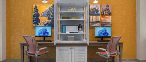A workspace with two desks, each with a computer monitor, a chair, and a white shelving unit with books and decorative items.
