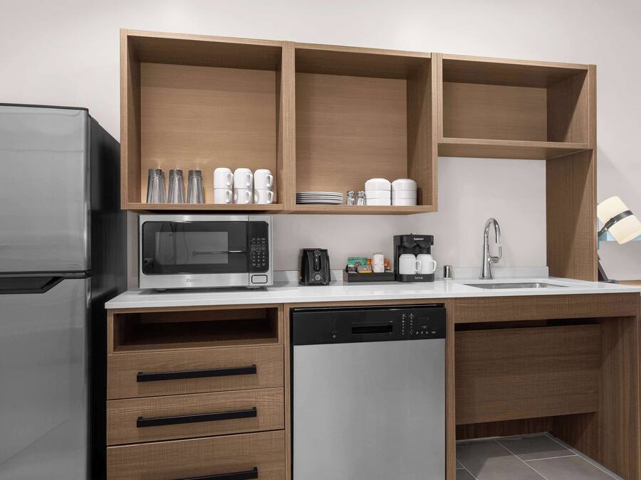 Cozinha compacta com micro-ondas embutido, cafeteira e máquina de lavar louça.