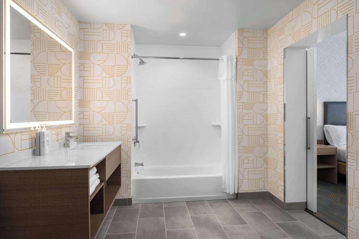 A modern bathroom with a bathtub, a vanity with a mirror, and patterned wallpaper.