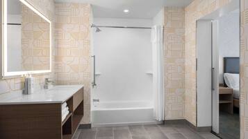 A modern bathroom with a bathtub, a vanity with a mirror, and patterned wallpaper.