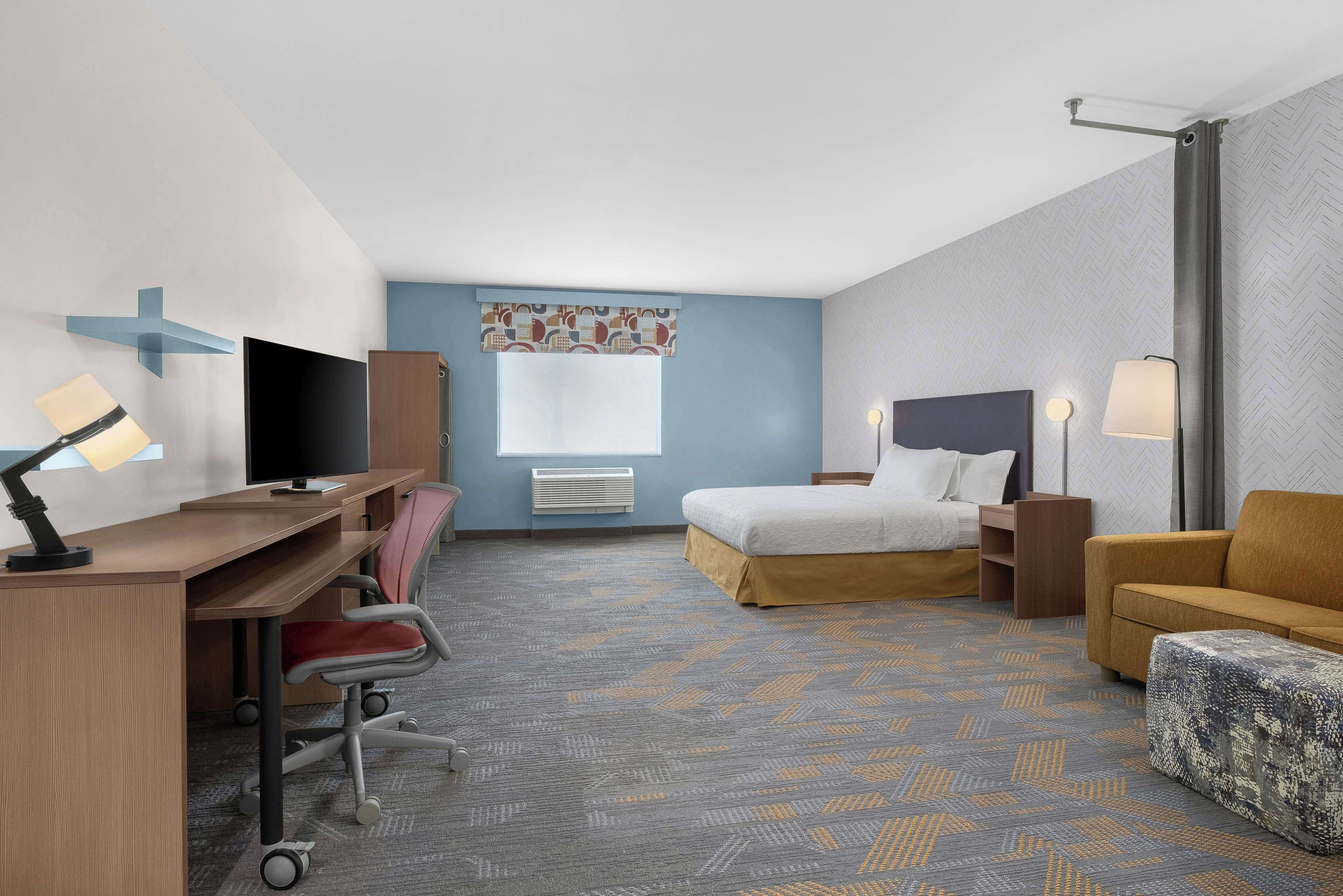 A hotel room with a desk, chair, bed, and sofa.
