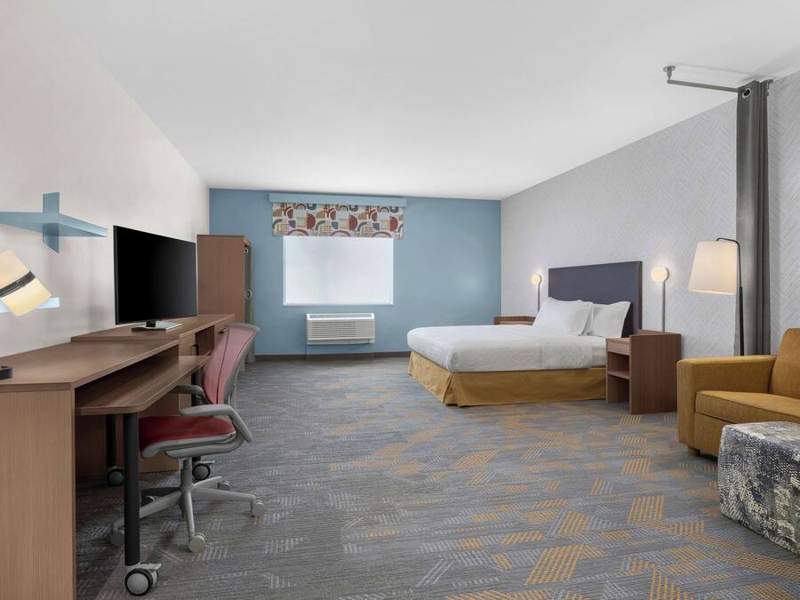A hotel room with a desk, chair, bed, and sofa.