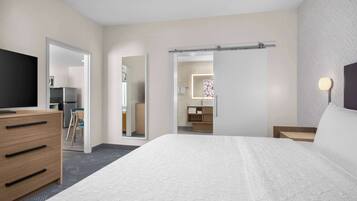 Una habitación de hotel moderna con una cama grande, un aparador de madera, un televisor y un baño visible a través de una puerta abierta.