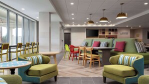 A modern lounge area with green upholstered chairs, a herringbone-patterned floor, and a large window providing natural light. - Home2 Suites By Hilton Winter Haven (Winter Haven)