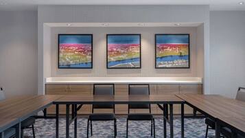 A conference room with a long table, six chairs, and three framed artworks on the wall.