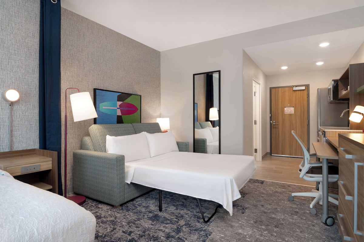 Een hotelkamer met een bed, een bureau, een stoel, een bank, een spiegel en een schilderij aan de muur.