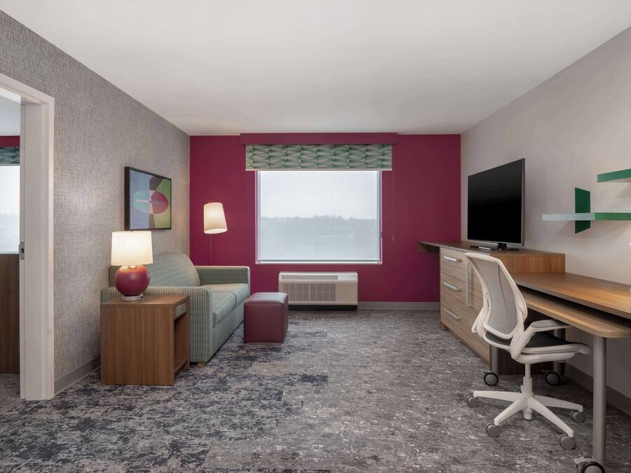 A hotel room with a bed, a desk, a chair, a TV, a lamp, and a window with a view.