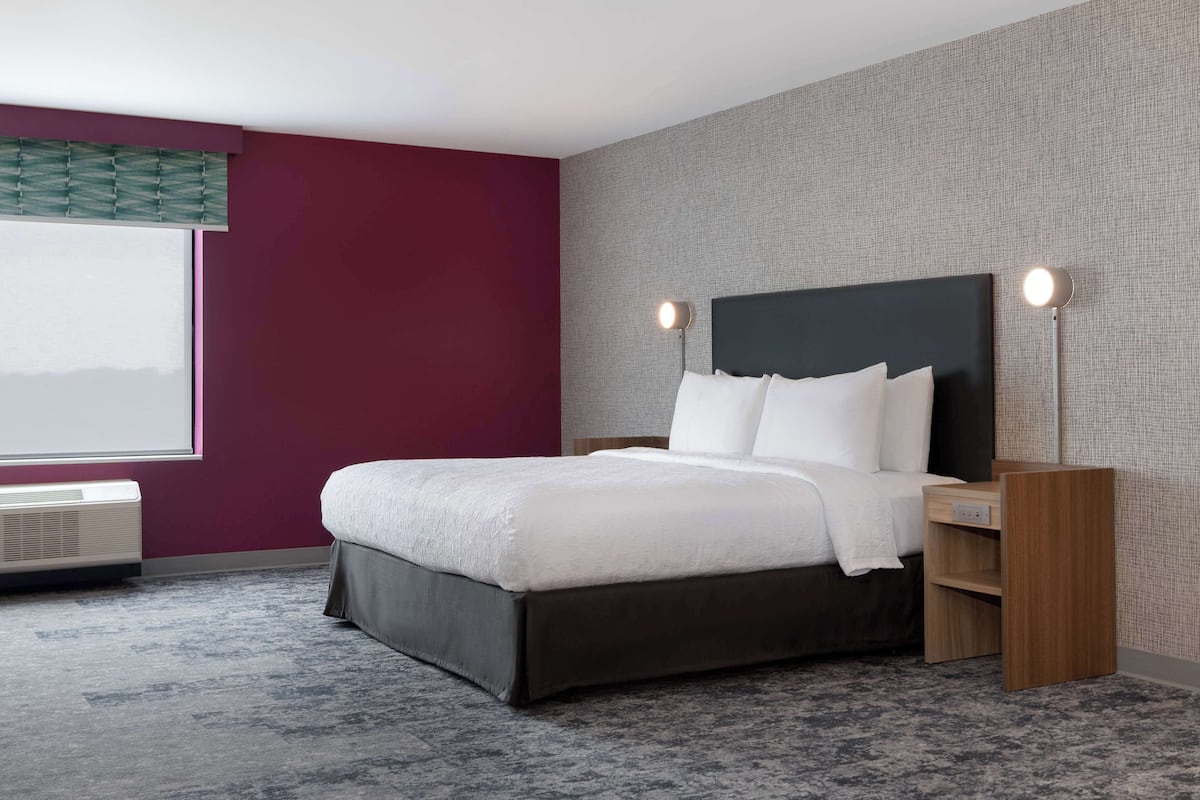Een moderne hotelkamer met een groot bed, een nachtkastje, een raam met uitzicht en een airconditioning.