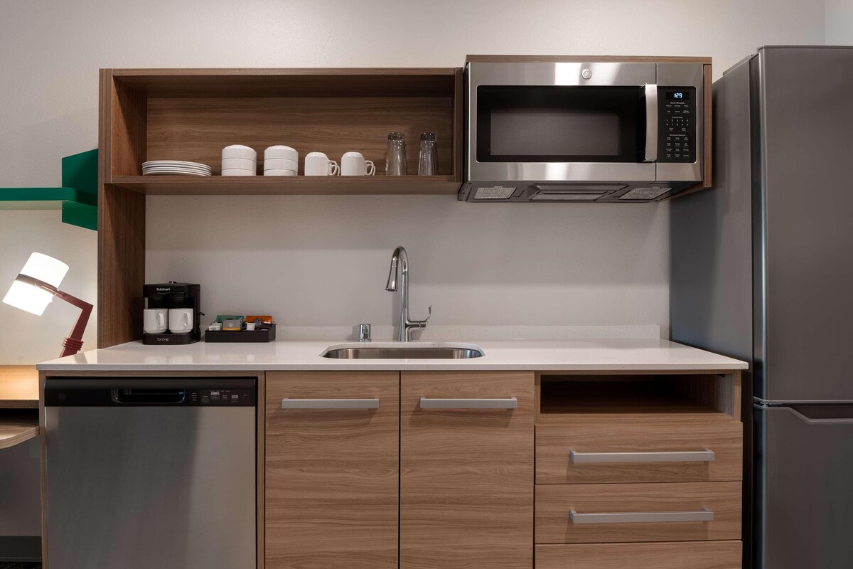 A modern kitchen with a built-in microwave, stainless steel refrigerator, and wooden cabinets.