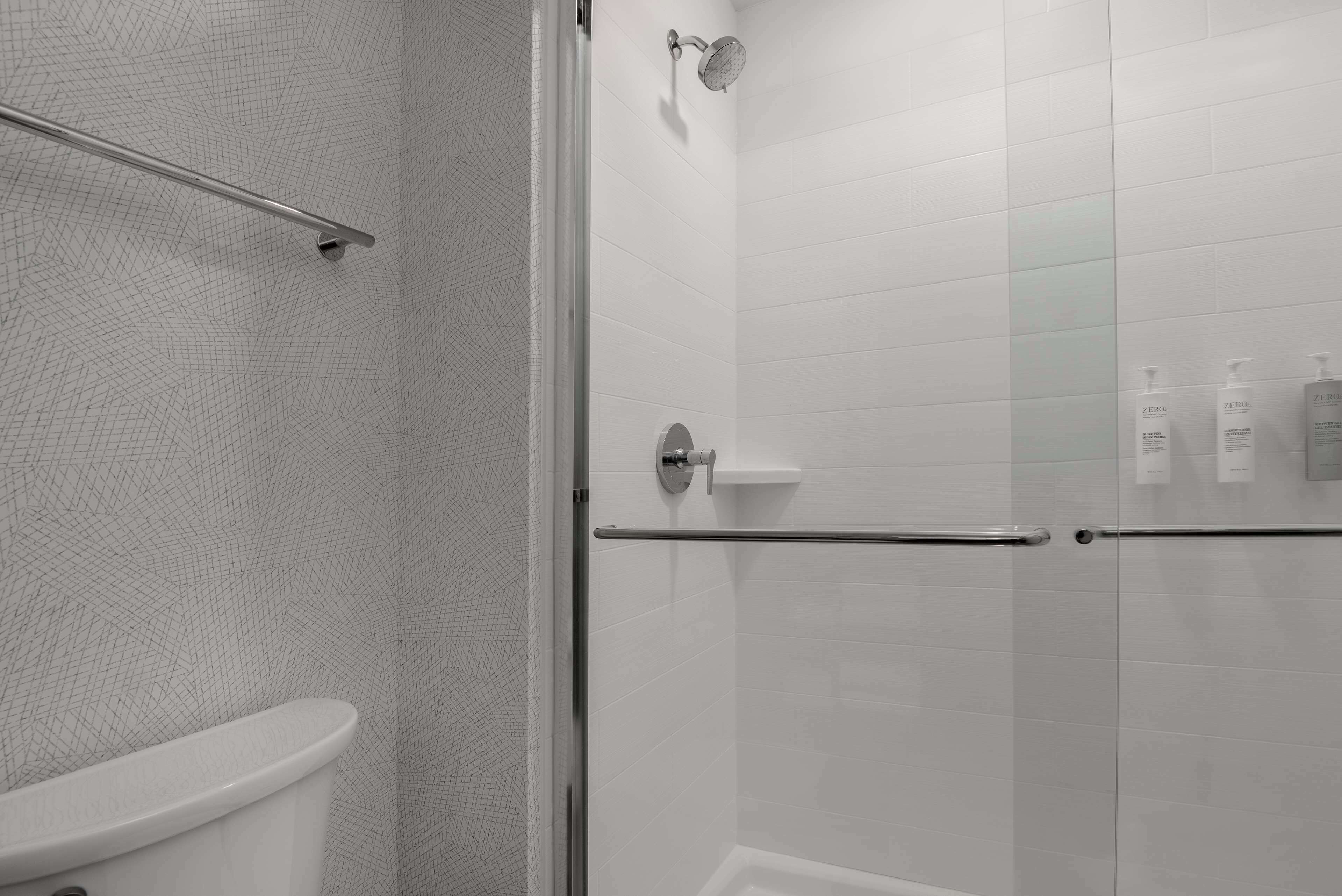 A modern bathroom with a glass shower enclosure, a toilet, and a hand dryer.