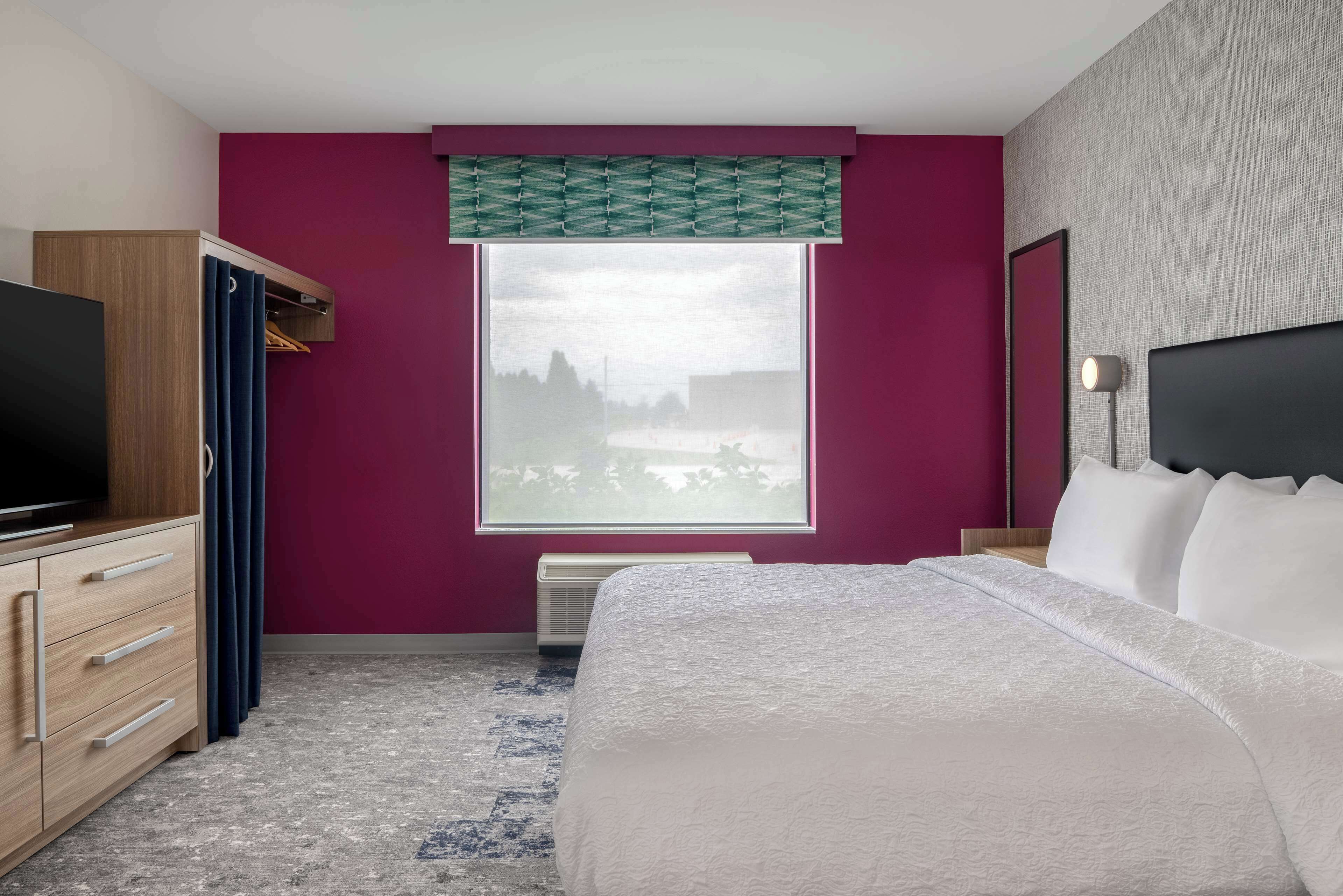 A hotel room with a bed, a TV, a wardrobe, a window with a view, and a bedside lamp.