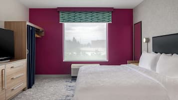 A hotel room with a bed, a TV, a wardrobe, a window with a view, and a bedside lamp.