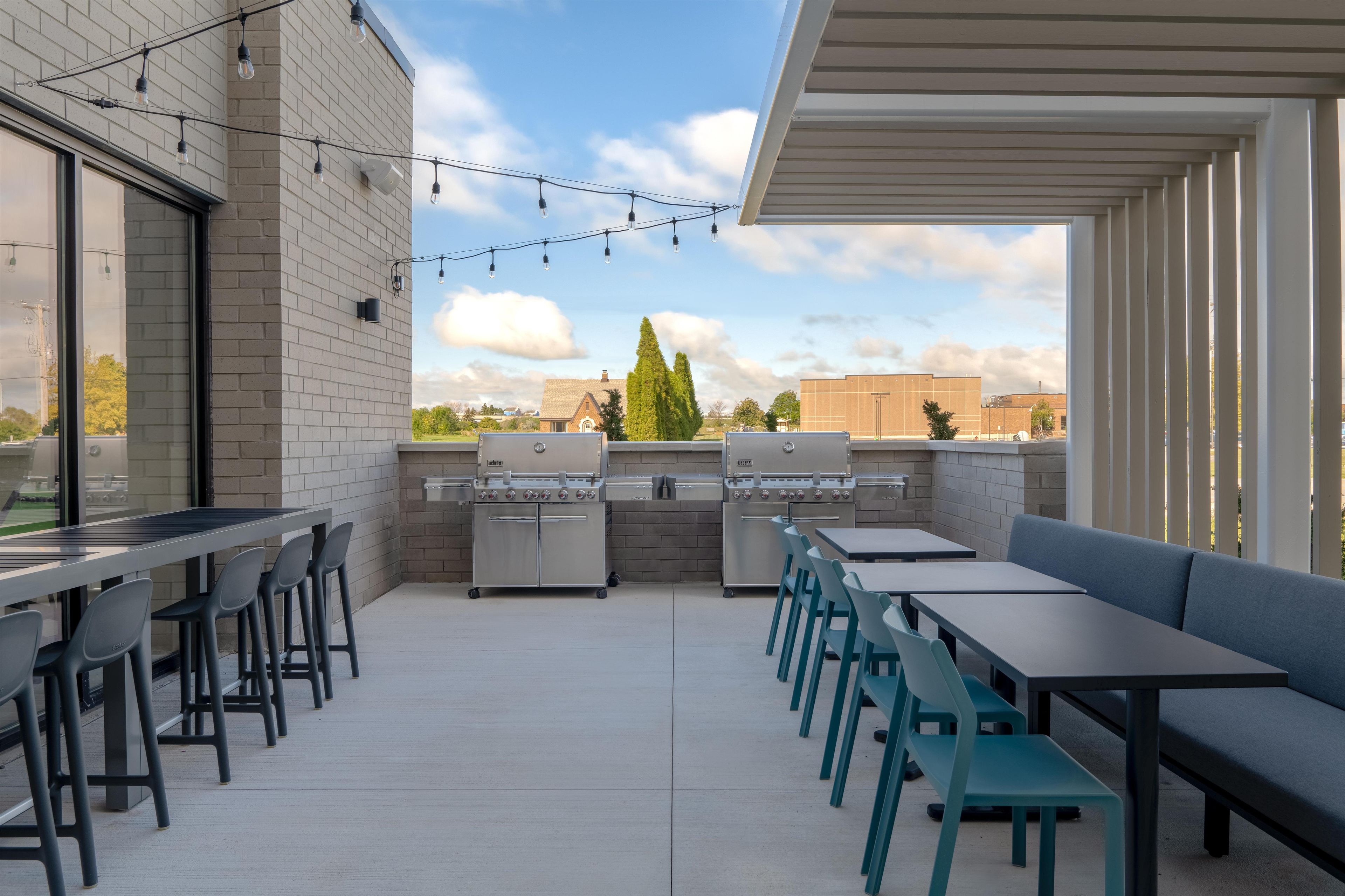 An outdoor patio with a grill, seating, and string lights.