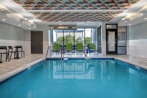 Una piscina interior con un diseño geométrico en el techo, una zona de estar con sillones y vistas al exterior a través de amplias ventanas.