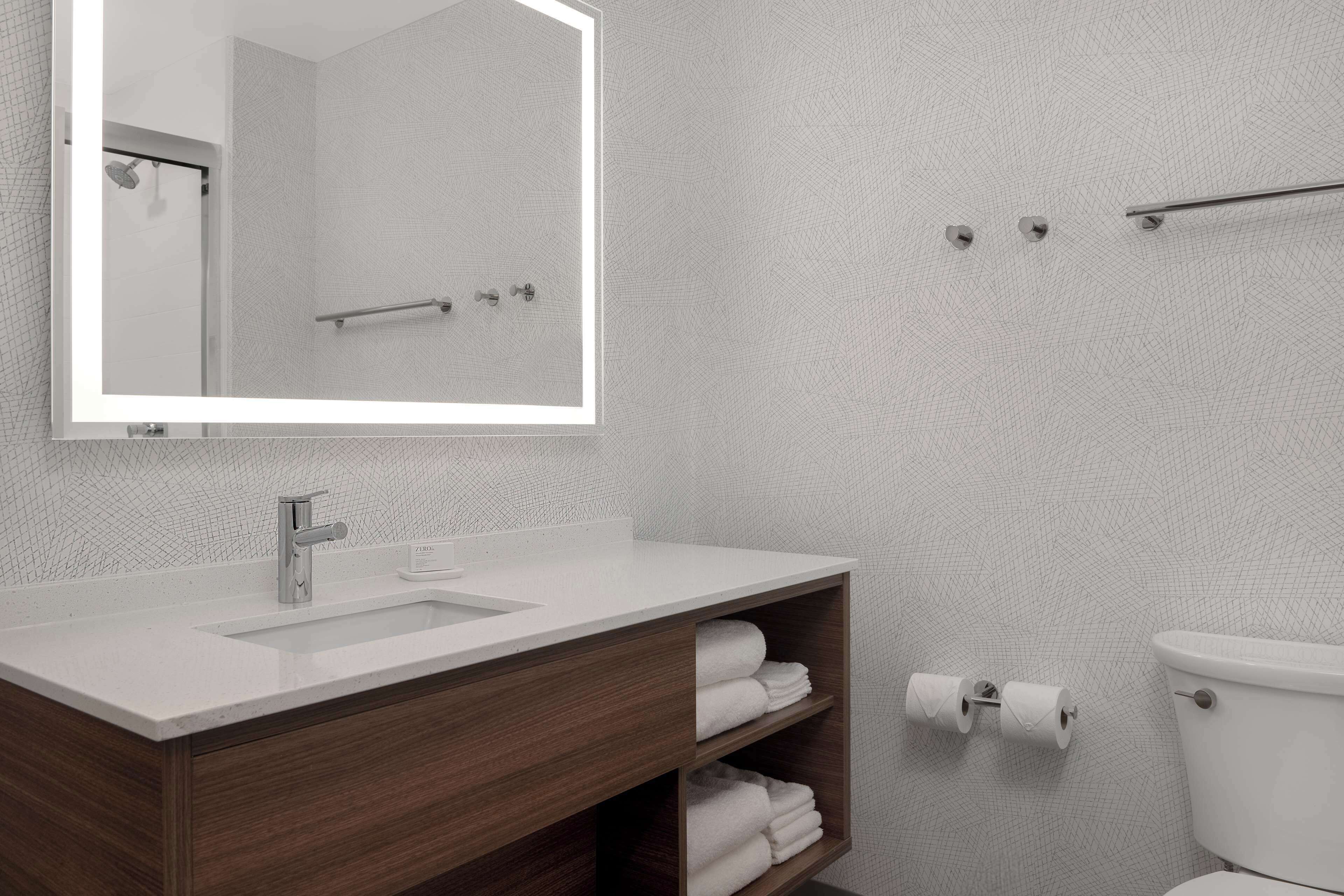 A bathroom with a white sink, wooden vanity, a mirror, a toilet, and a towel rack.