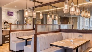 Un café moderne avec des tables en bois et des banquettes rembourrées, un espace dédié au café et des luminaires suspendus.