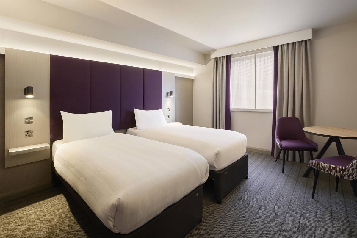 Une chambre d’hôtel avec deux lits, un bureau, une chaise et une fenêtre avec des rideaux.