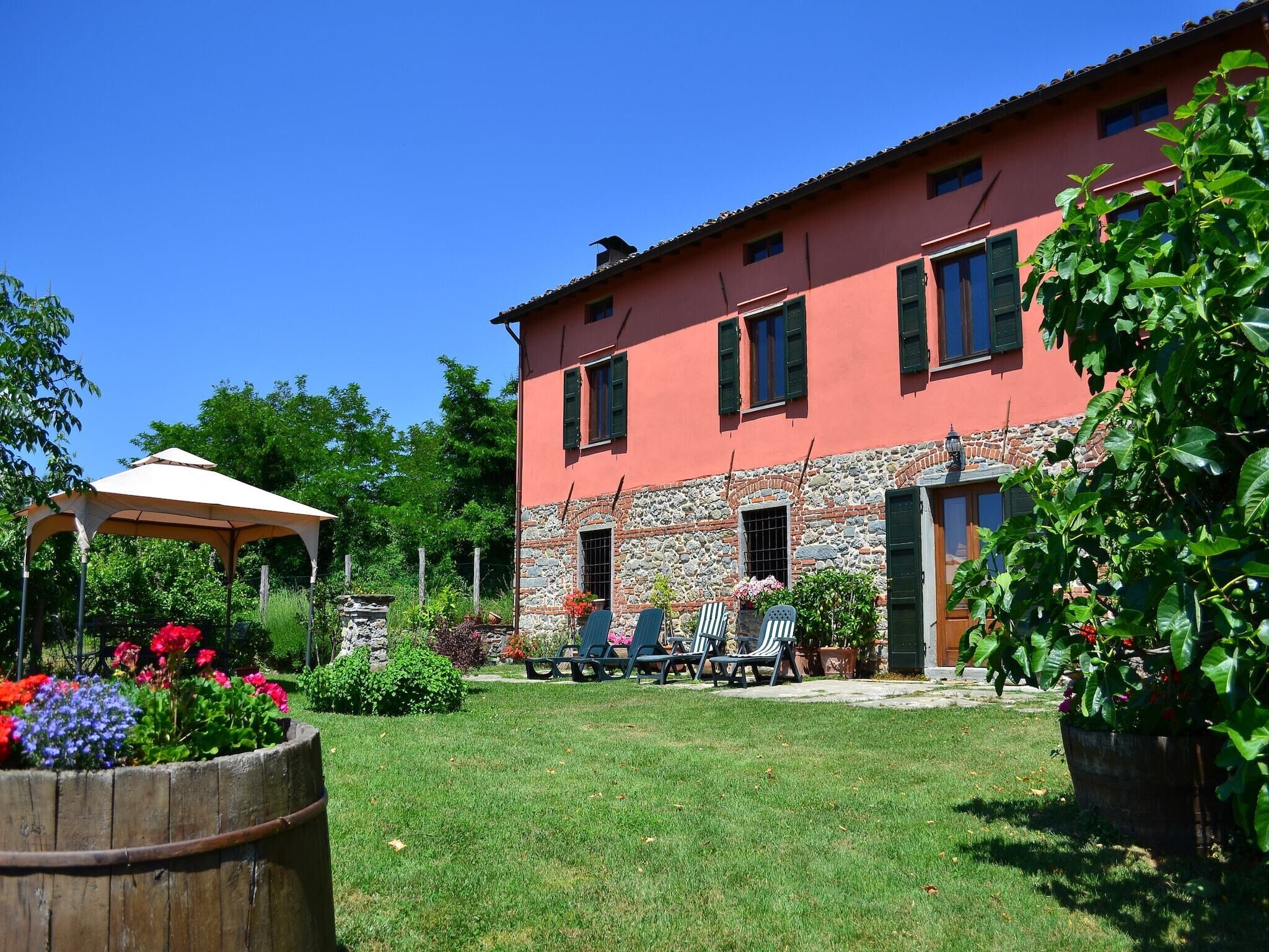 Il s’agit d’un bâtiment à deux étages, doté d’une façade en pierre et d’une couleur rouge. On y trouve un patio avec une table et des chaises, ainsi qu’un jardinier en bois rempli de fleurs.