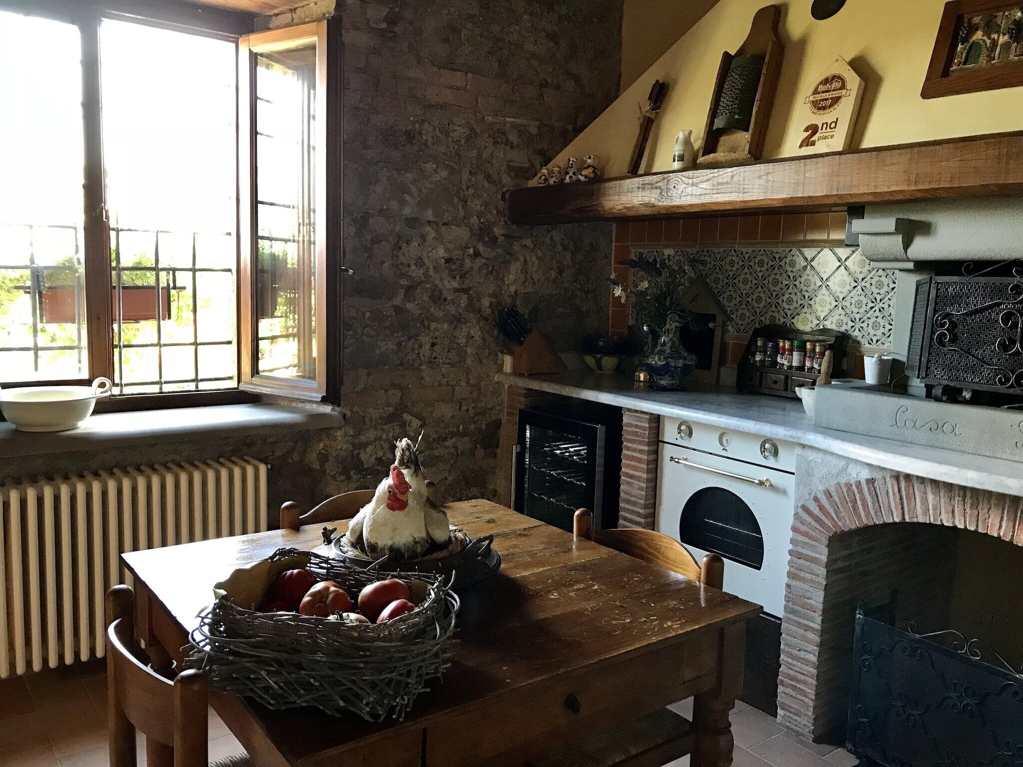Una cucina rustica con un muro in pietra, un tavolo di legno con un cesto di uova, un forno bianco e una finestra vista verde.