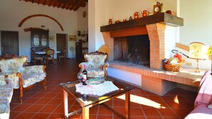 A cozy living room with a fireplace, wooden beams, and floral-patterned furniture. - Agriturismo in Tuscany with Pool and Wine Tasting (Peccioli)
