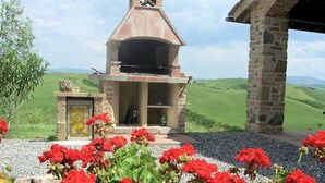 A stone building with a chimney, surrounded by red flowers and a grassy landscape. - Agriturismo in Tuscany with Pool and Wine Tasting (Peccioli)