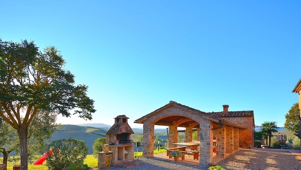 A stone-built outdoor structure with a covered seating area, surrounded by gravel and potted plants, overlooking a scenic landscape. - Agriturismo in Tuscany with Pool and Wine Tasting (Peccioli)