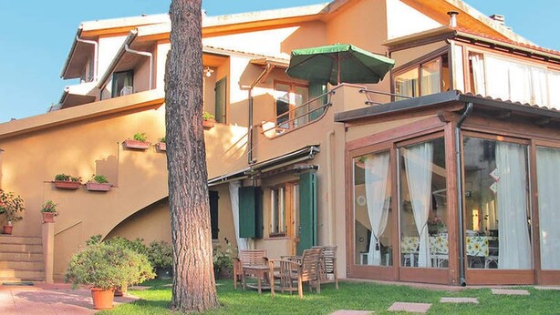 Una casa de dos plantas con un balcón, un amplio ventanal corredero y un pequeño patio con sillas y una mesa.